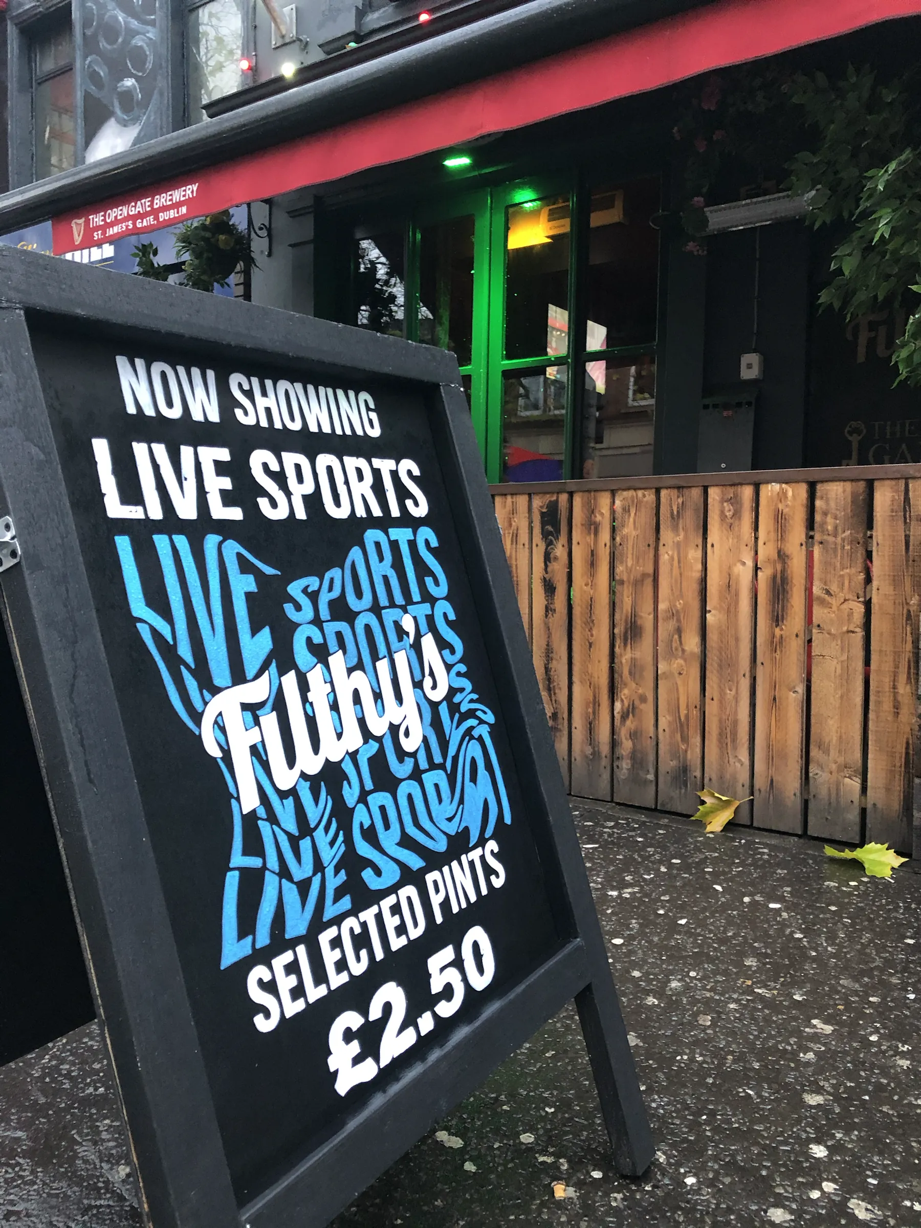 A black A-board outside Filthy’s advertising live sports and selected pints at £2.50, with “Live sports” repeated in blue lettering behind the Filthy’s logo.