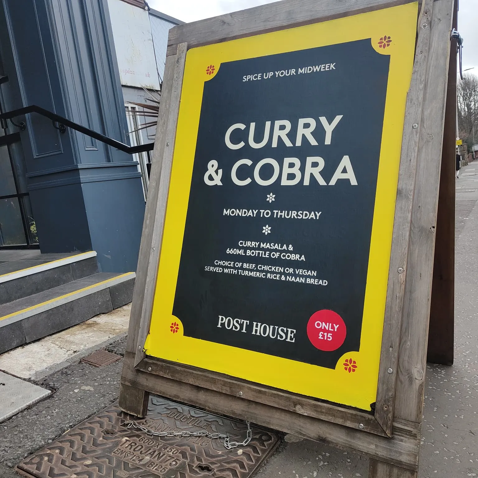 A wooden A-board outside the Post House with a yellow-bordered navy panel advertising “Curry & Cobra”, Monday to Thursday, for £15.