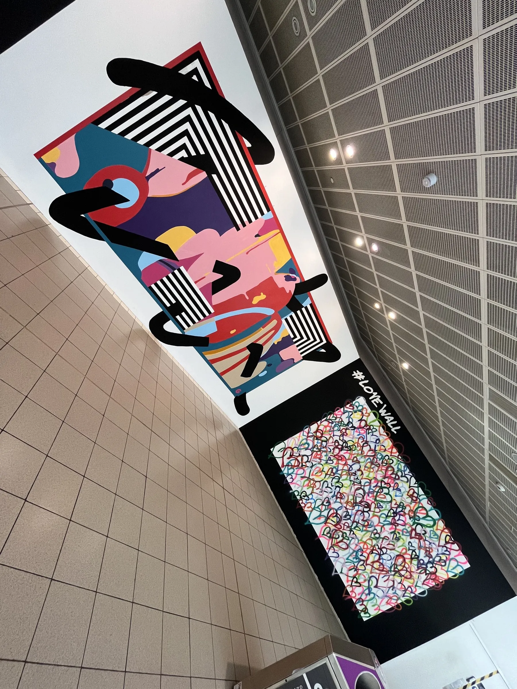 Looking up along the abstract mural and the #LoveWall from the floor, the centre’s ceiling grid above.