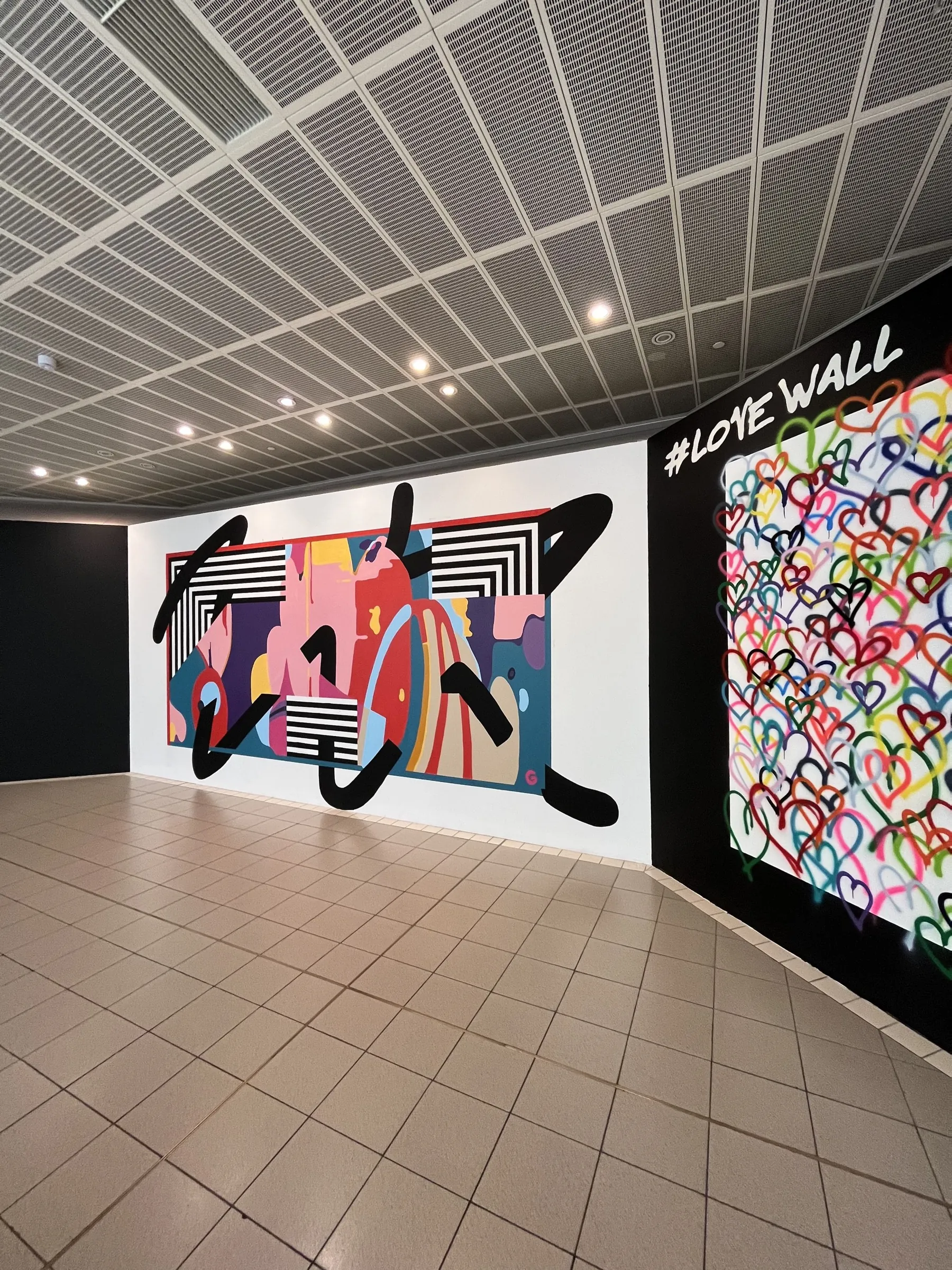 Looking along the finished abstract mural on its white wall, the #LoveWall turning the corner beside it.