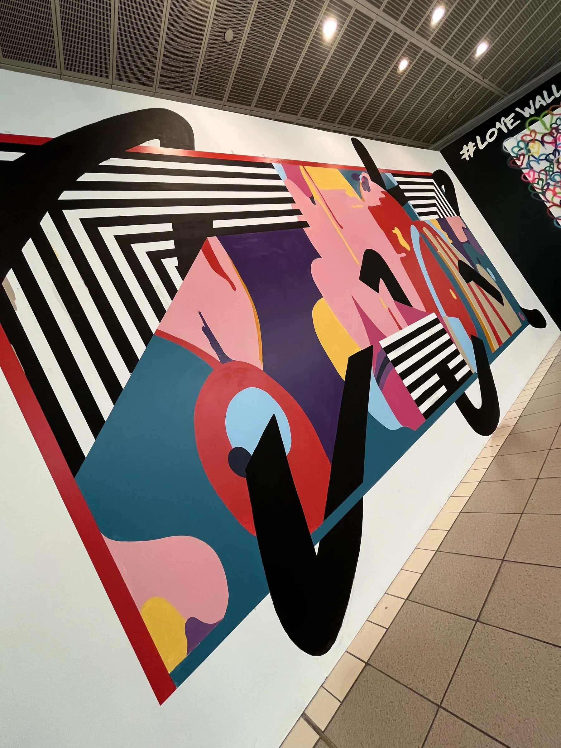 The abstract mural seen up close at an angle, black brush strokes sweeping over its striped and colour-blocked panel.