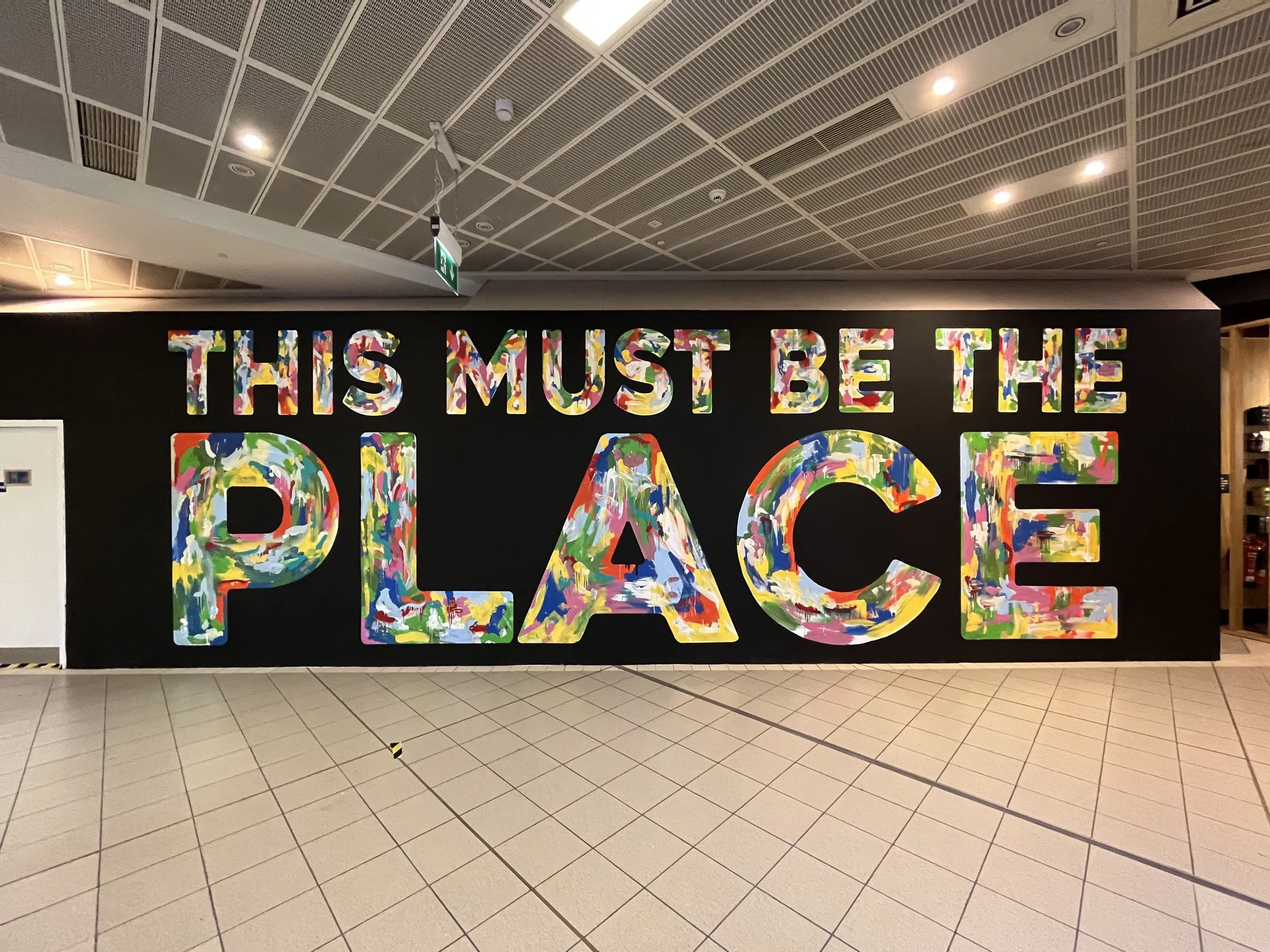 “This must be the place” in giant capitals on a black hoarding, each letter filled with multicoloured brushwork.