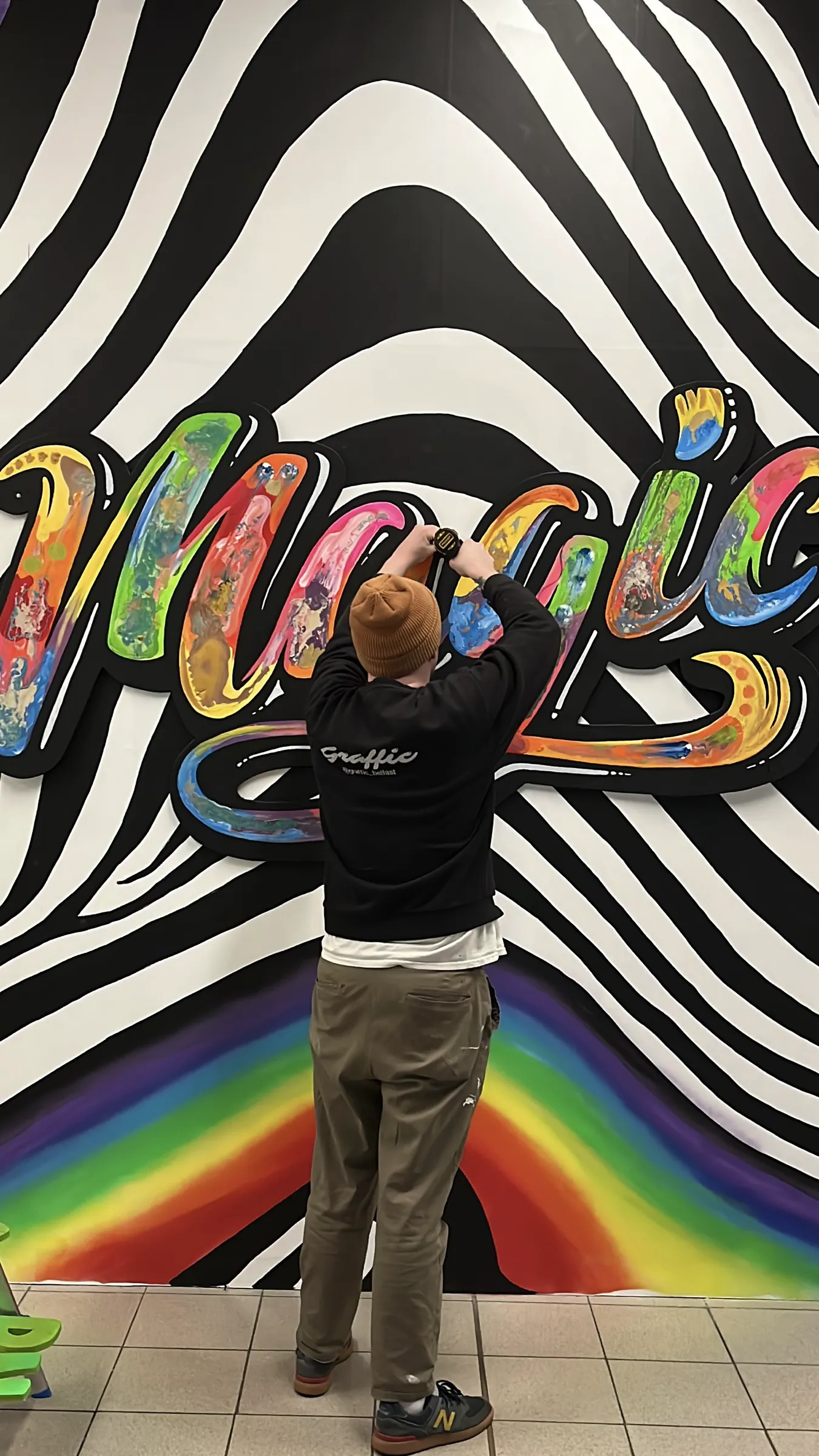 A Graffic painter filling in rainbow “Magic” lettering over a black and white zebra-stripe pattern.