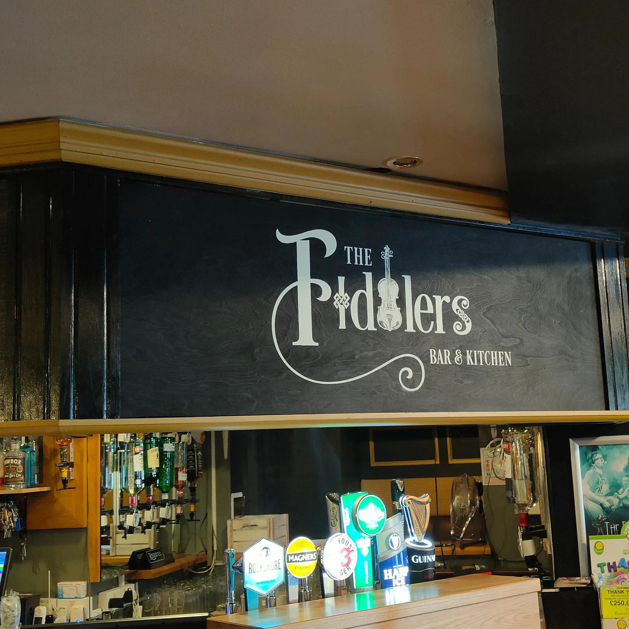 “The Fiddlers, Bar & Kitchen” hand-lettered in cream on a dark panel above the bar.