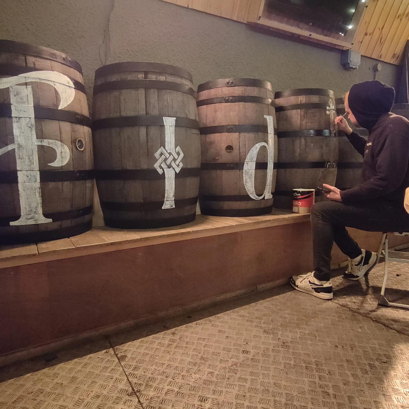 A painter lettering a giant “F” across a row of whiskey barrels.