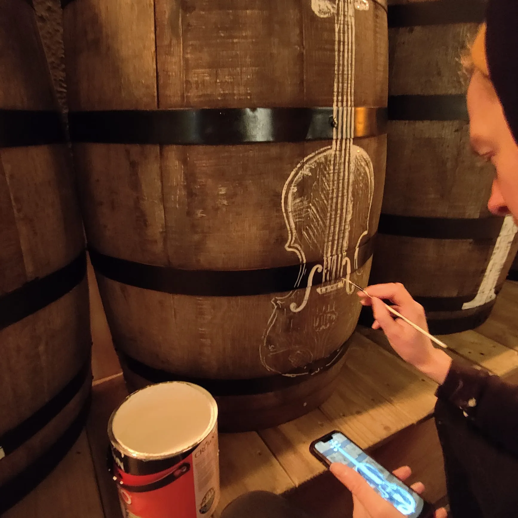 A close-up of a fiddle being painted in cream on a whiskey barrel.