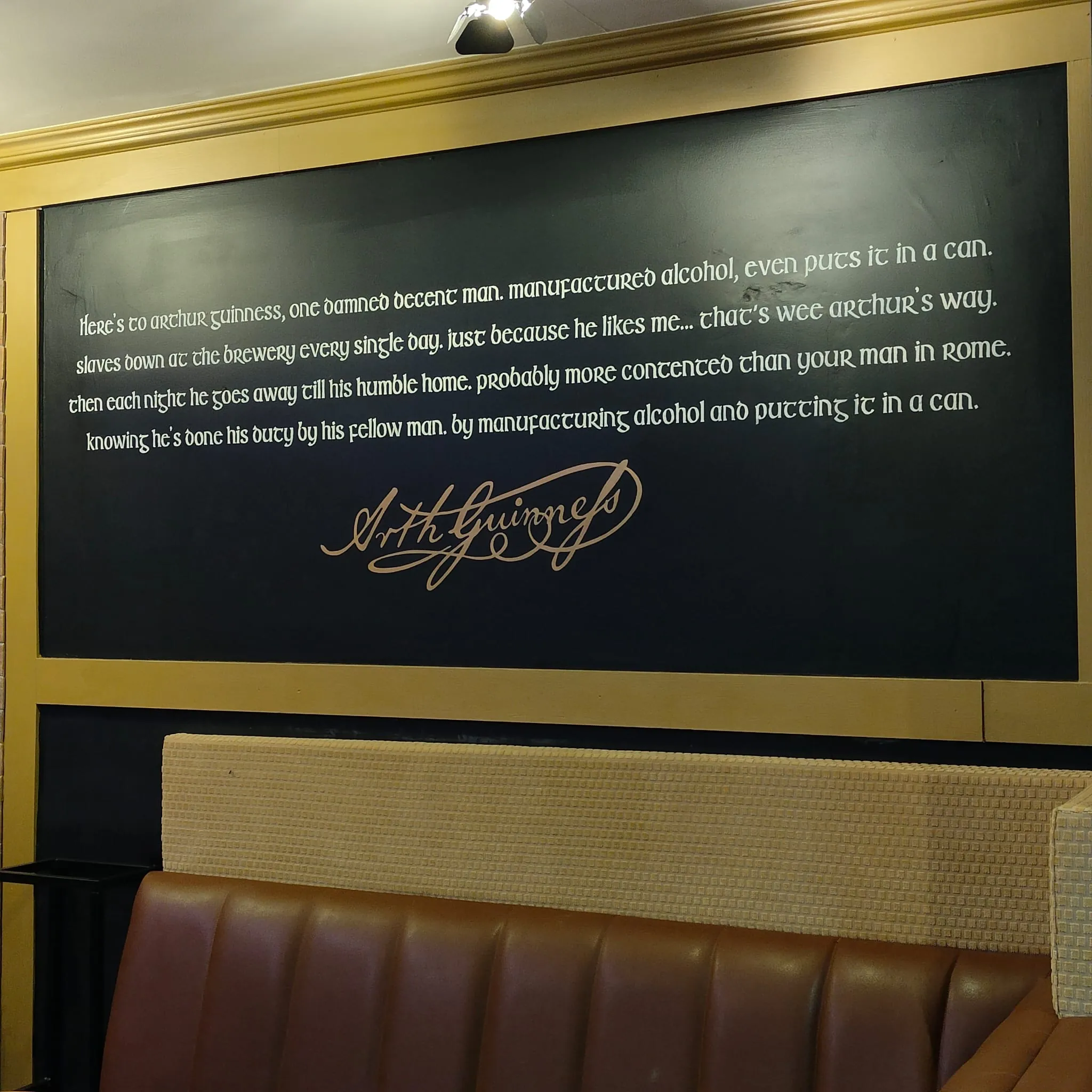 A Guinness quote and Arthur Guinness’s signature hand-lettered in white on a dark wall above a booth.