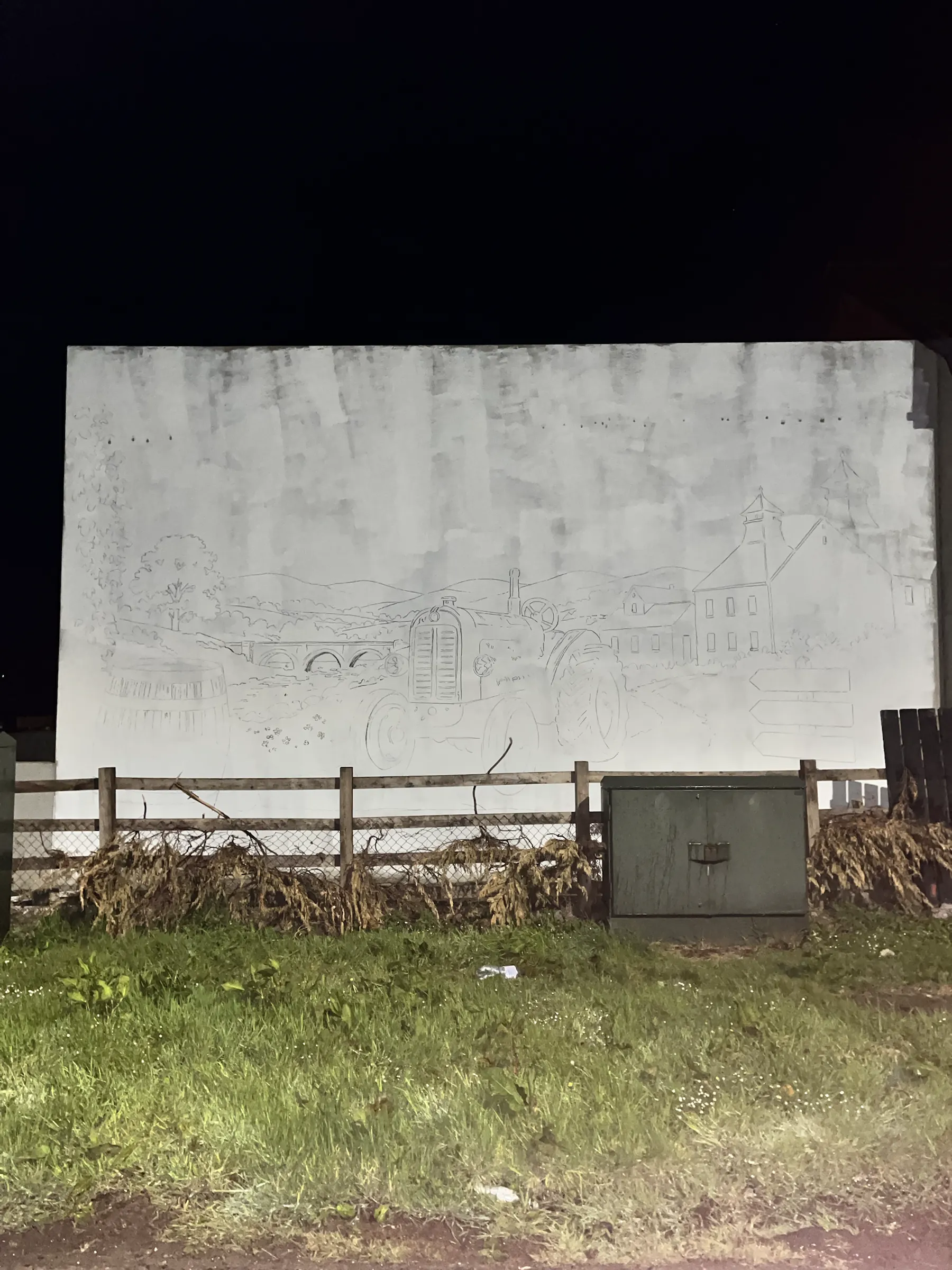 Pencil outlines of the Bushmills mural sketched across the gable at night.