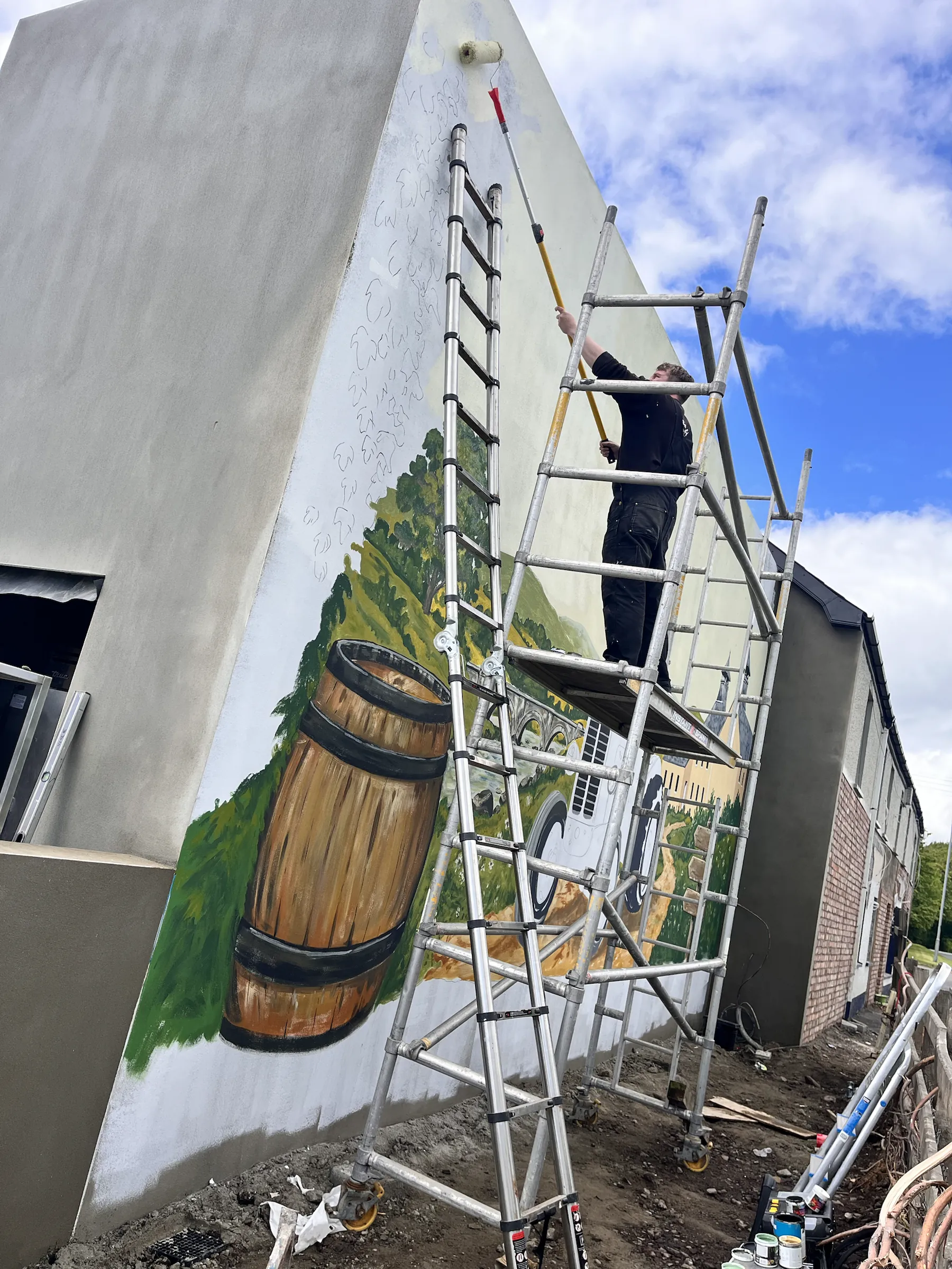 A painter up a ladder tower at the edge of the gable, beside the finished Bushmills barrel.