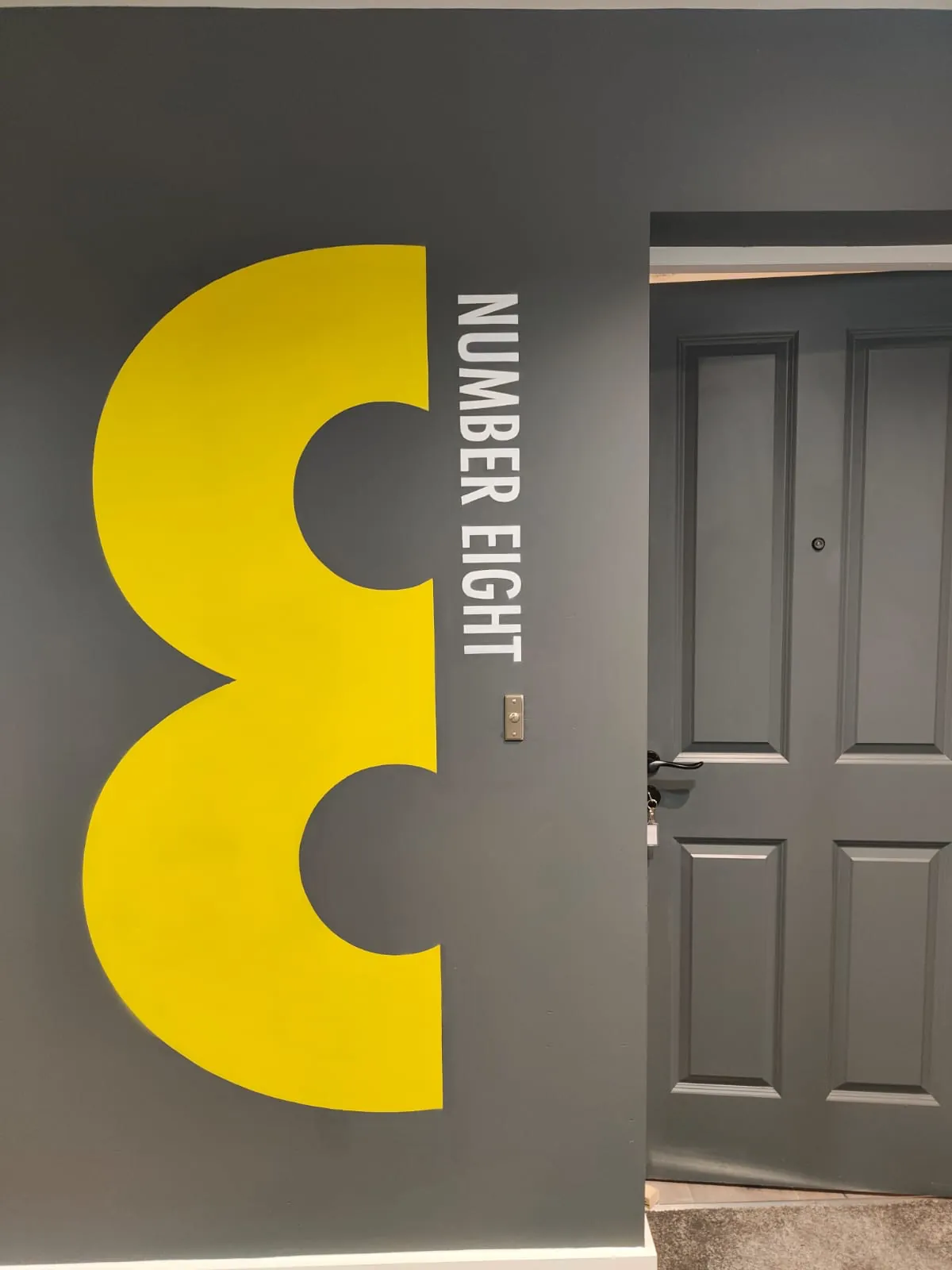 A giant yellow “8” painted beside a grey apartment door, with “Number eight” in white.