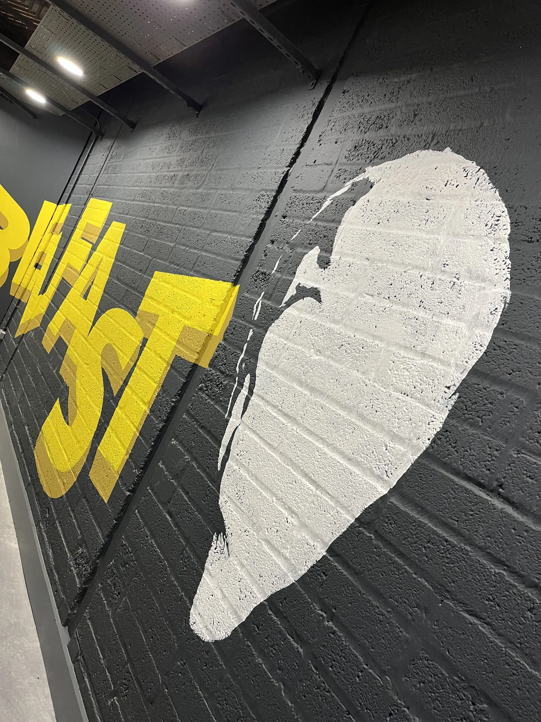 Bold yellow “Belfast” lettering beside a white painted face on a black brick wall.
