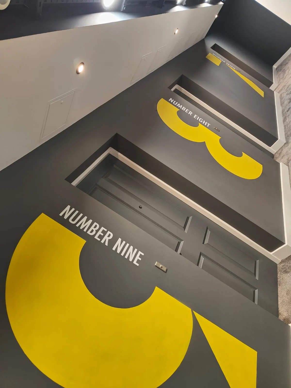 Giant yellow numerals painted on a dark grey landing beside the doors, labelled “Number nine” and “Number eight”.