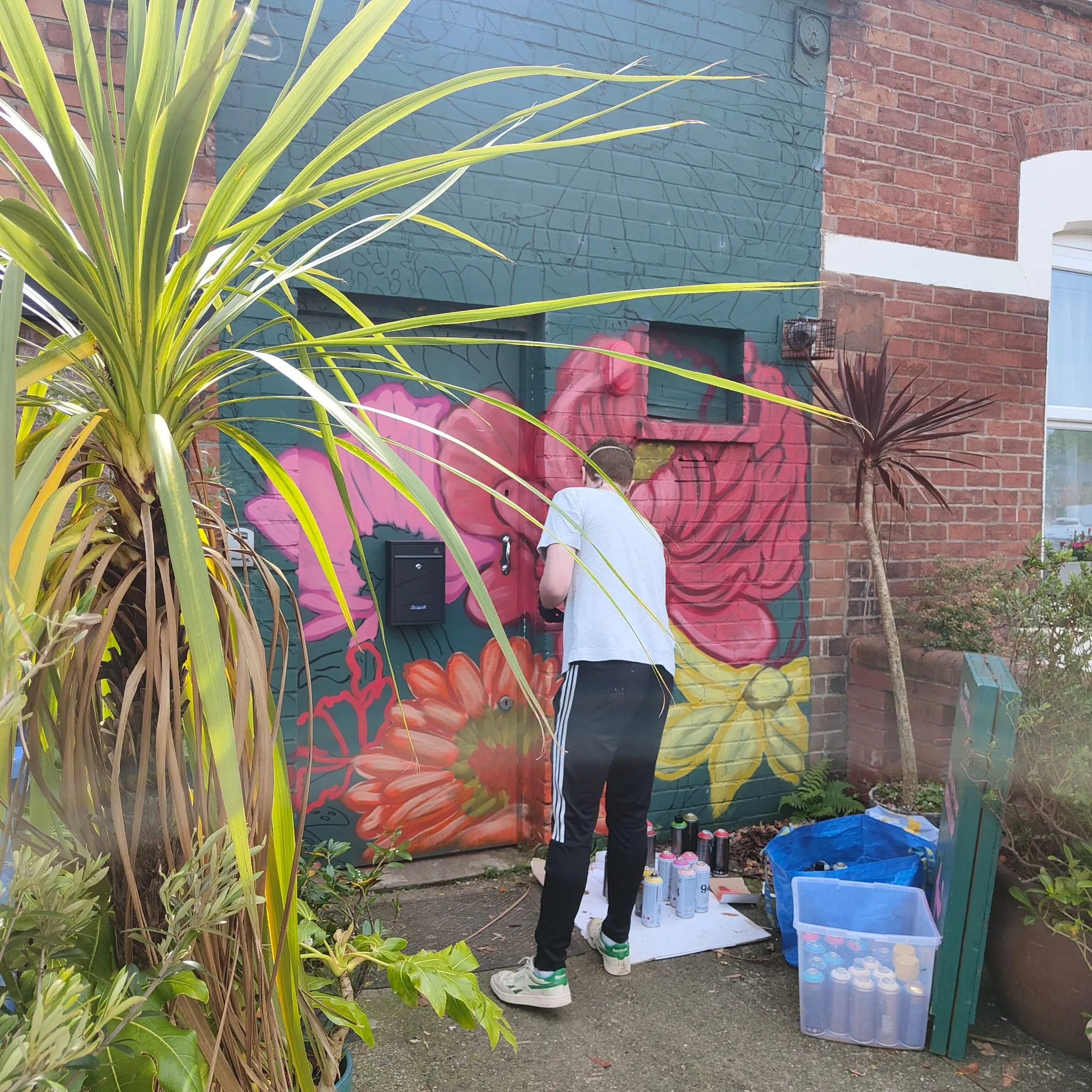 A painter at work on the floral mural behind the plants in Memento’s garden.