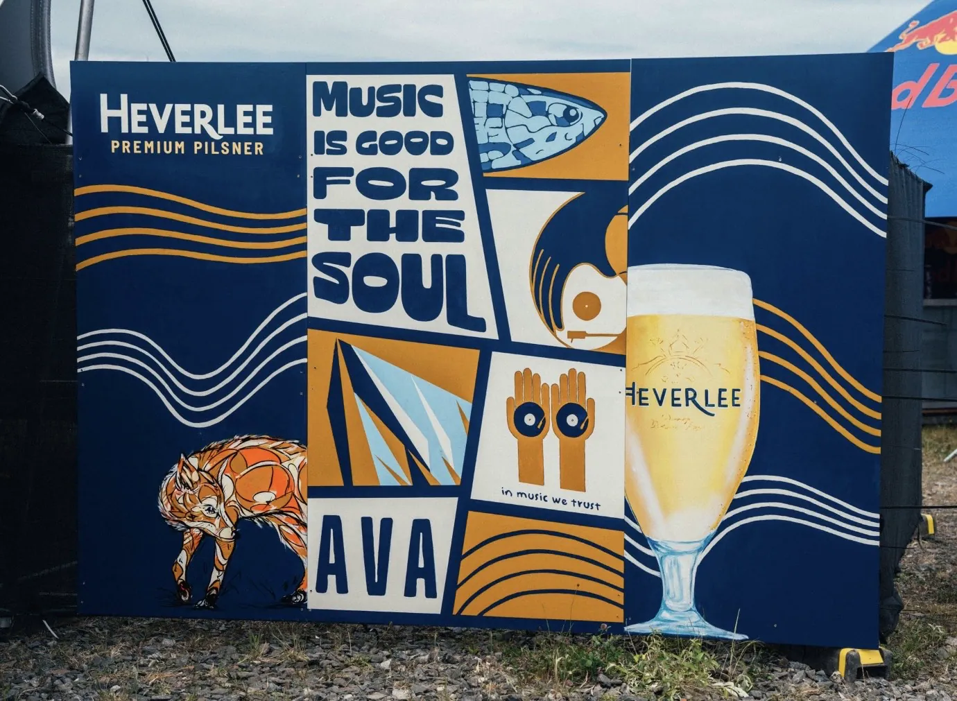 A festival hoarding painted for Heverlee at AVA, with blocks reading “Music is good for the soul”, a stag, a pair of hands and a glass of pilsner.