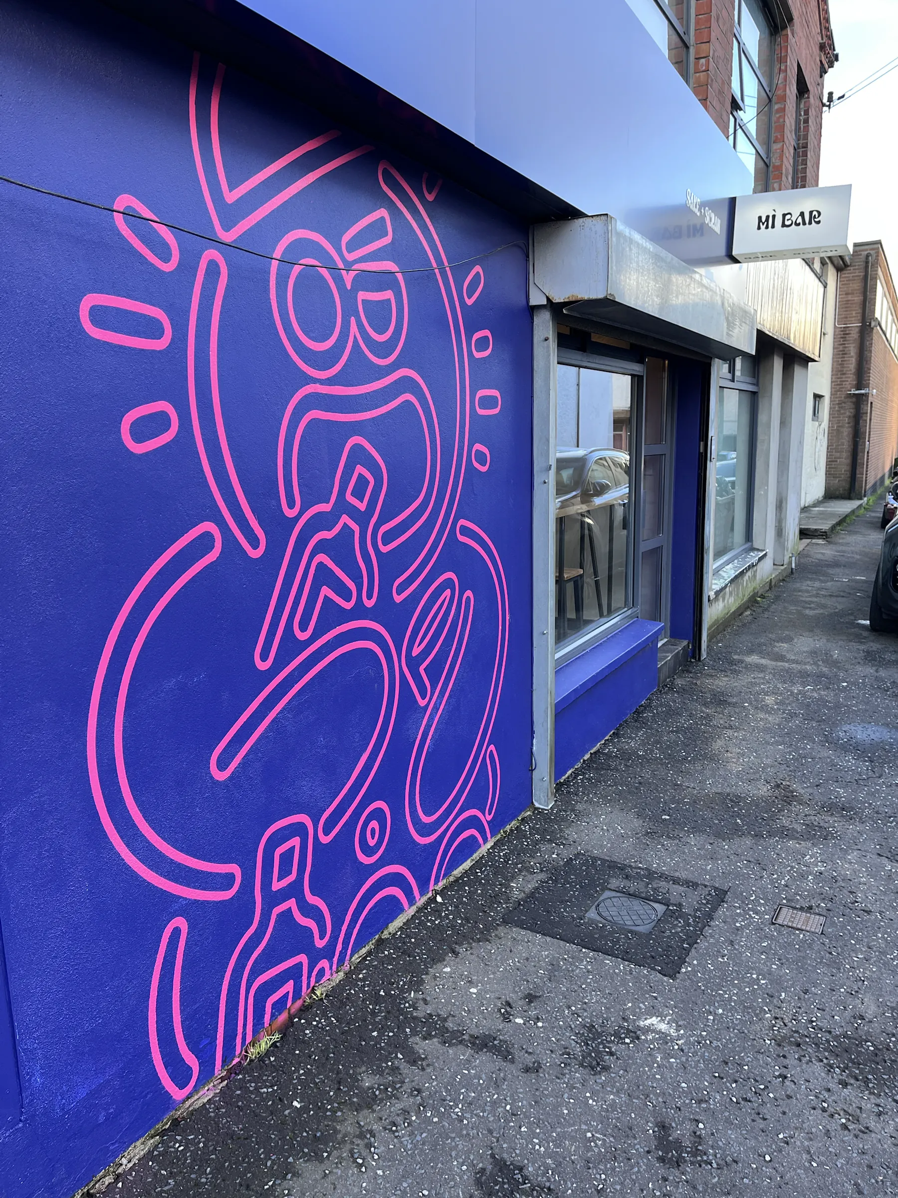 A wall painted deep blue with a large pink line drawing of a stylised figure, running along the street front beside the entrance to Hi Bar.