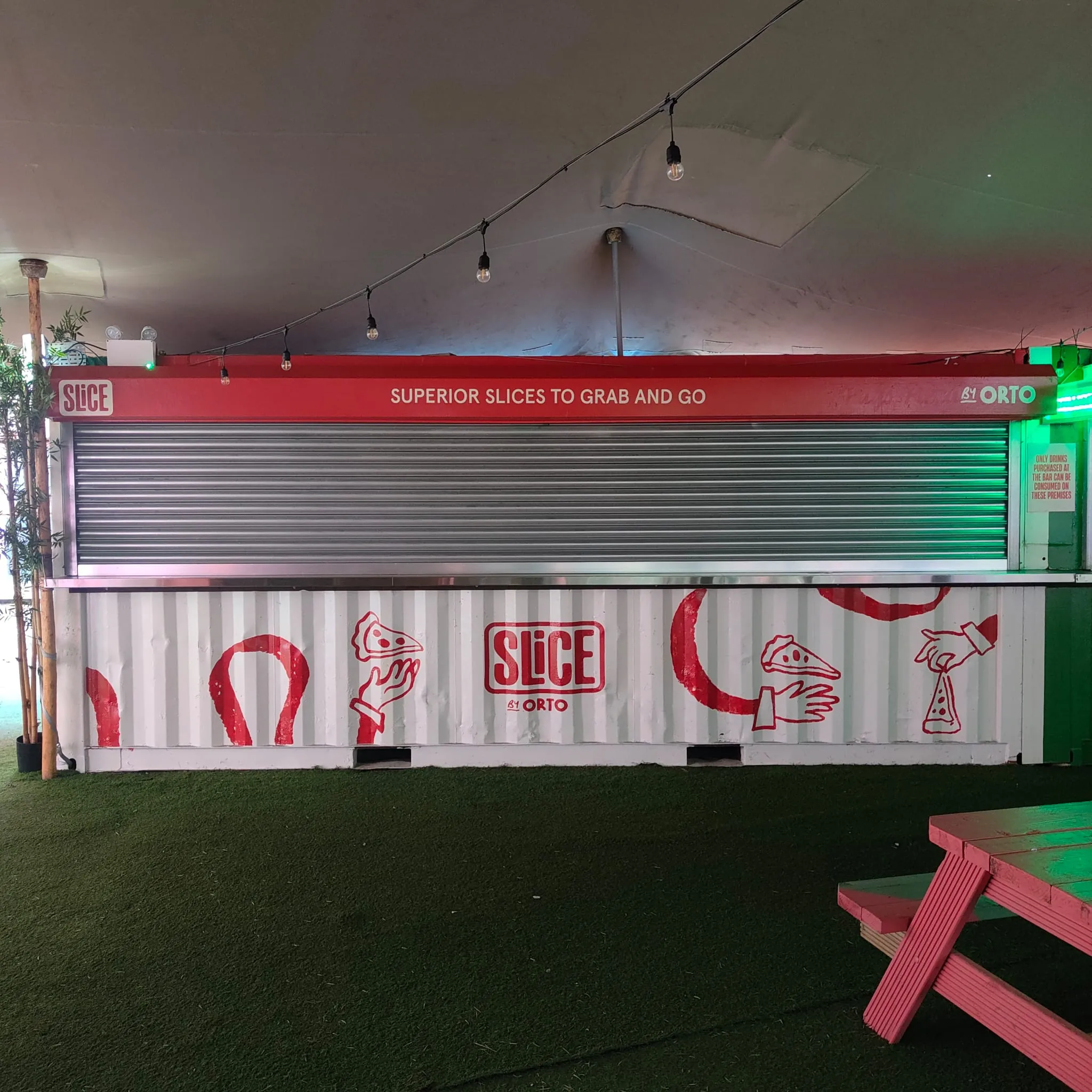 A shipping-container food stall for Slice by Orto, its fascia lettered “Superior slices to grab and go” and its side painted with red pizza-slice and horseshoe illustrations.