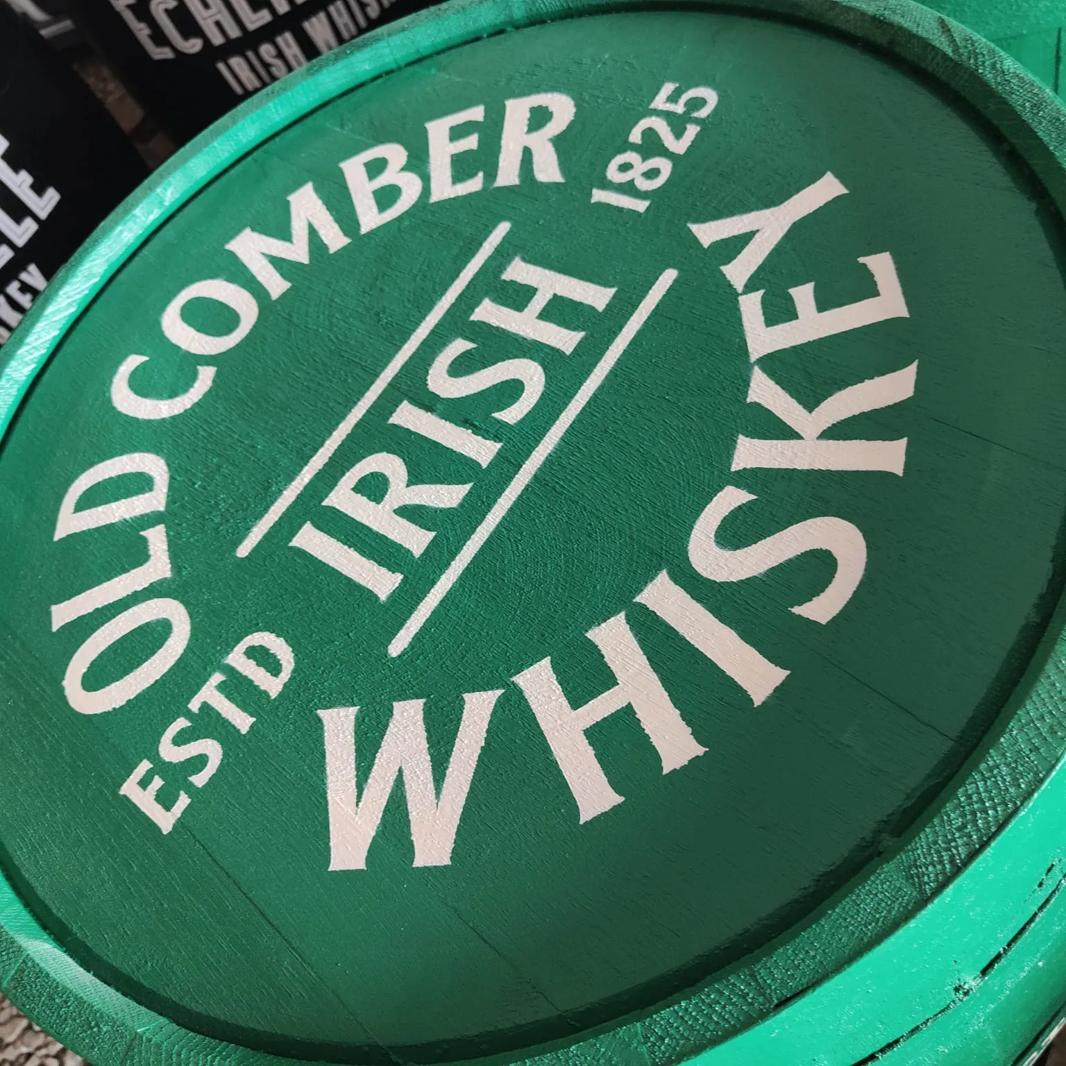 A green barrel head hand-lettered in white with “Old Comber Irish Whiskey, Estd 1825”.