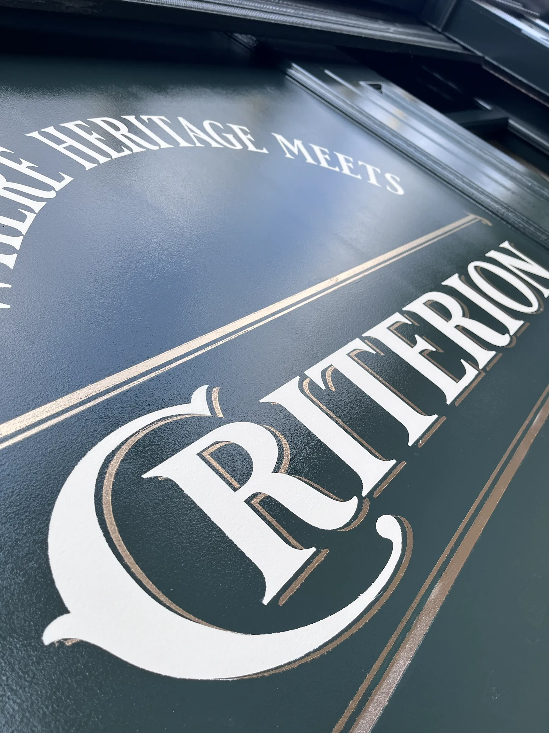 Cream serif lettering with a gold shadow reading “Criterion” on a dark green fascia, beneath the line “Where heritage meets”.