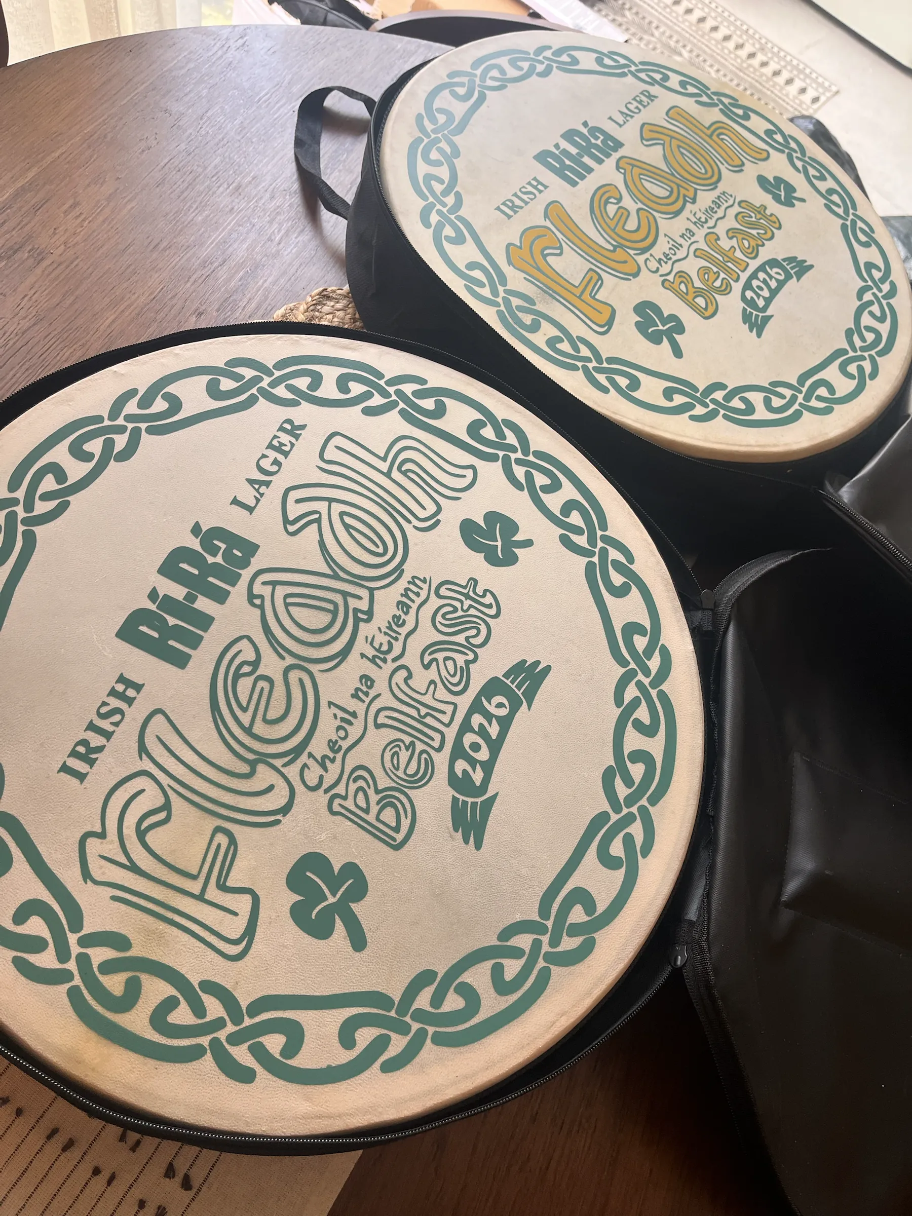 Two bodhráns hand-painted for Fleadh Cheoil na hÉireann in Belfast, with Celtic knotwork borders, shamrocks and Rí-Rá Irish Lager branding.