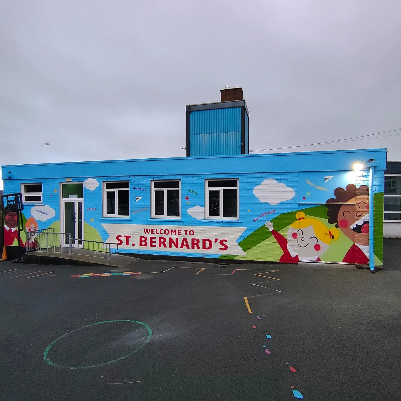 A school building painted bright blue with “Welcome to St. Bernard’s” and smiling cartoon children across its wall.