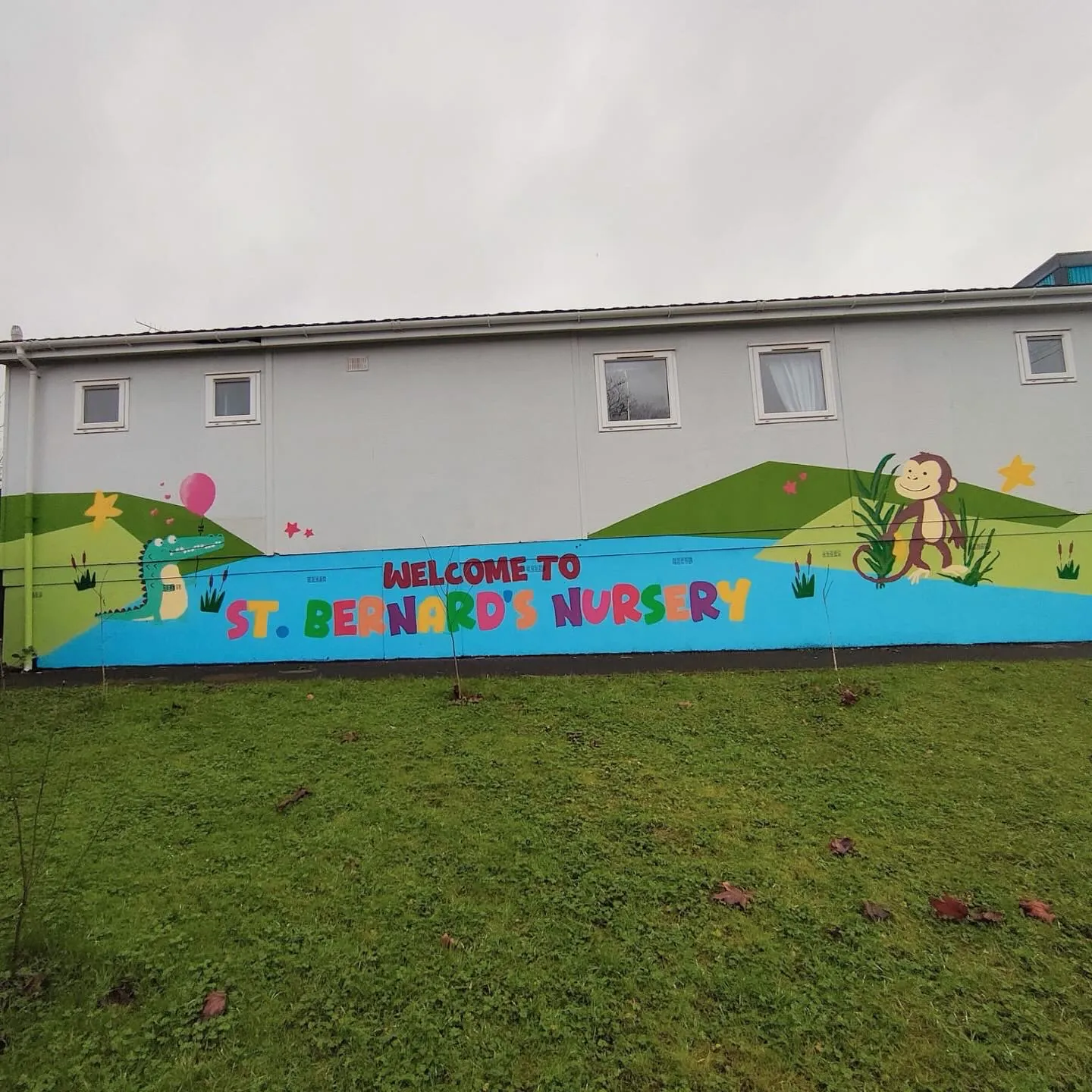 A long wall painted with green hills, a monkey and “Welcome to St. Bernard’s Nursery” across a blue band.