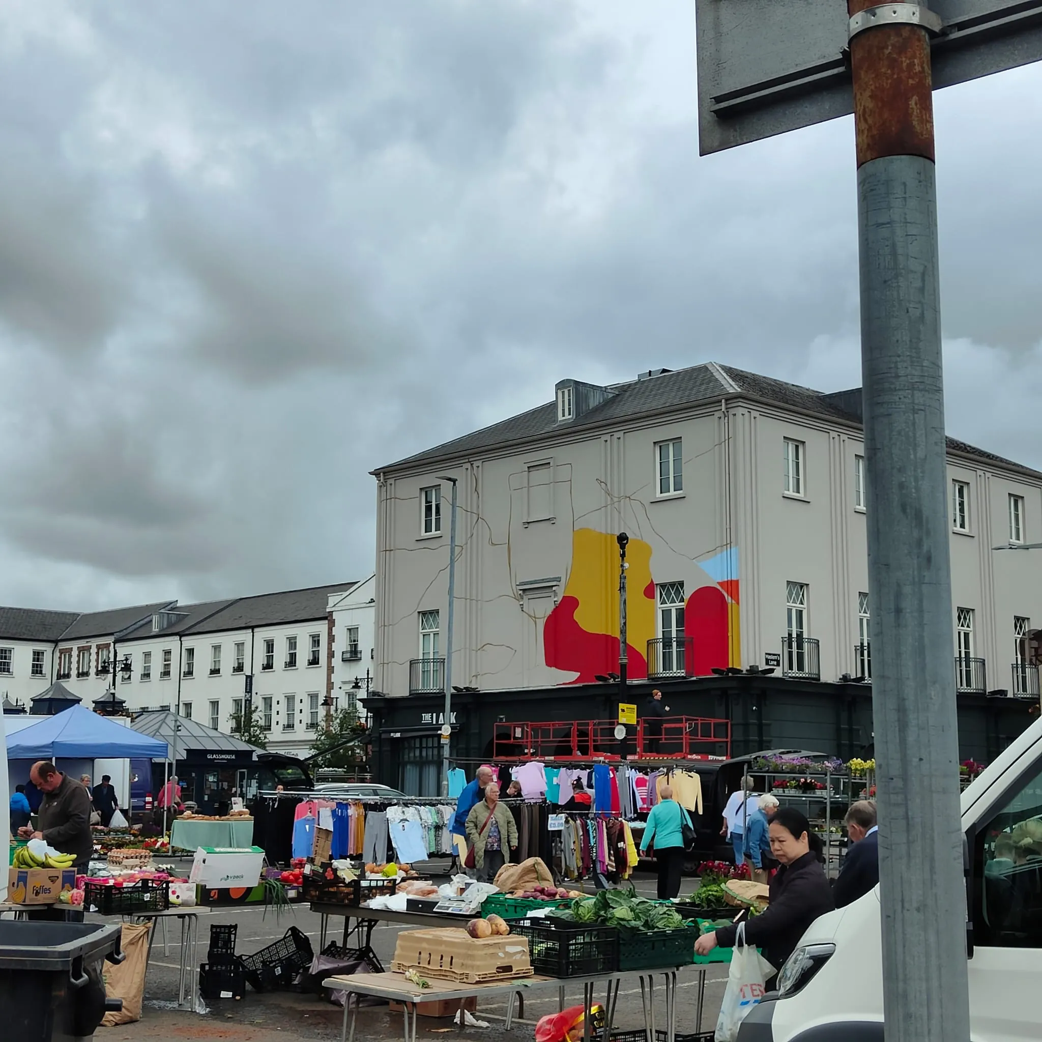 The Lark’s mural in progress above a busy outdoor market, its first red and yellow shapes on the white gable.