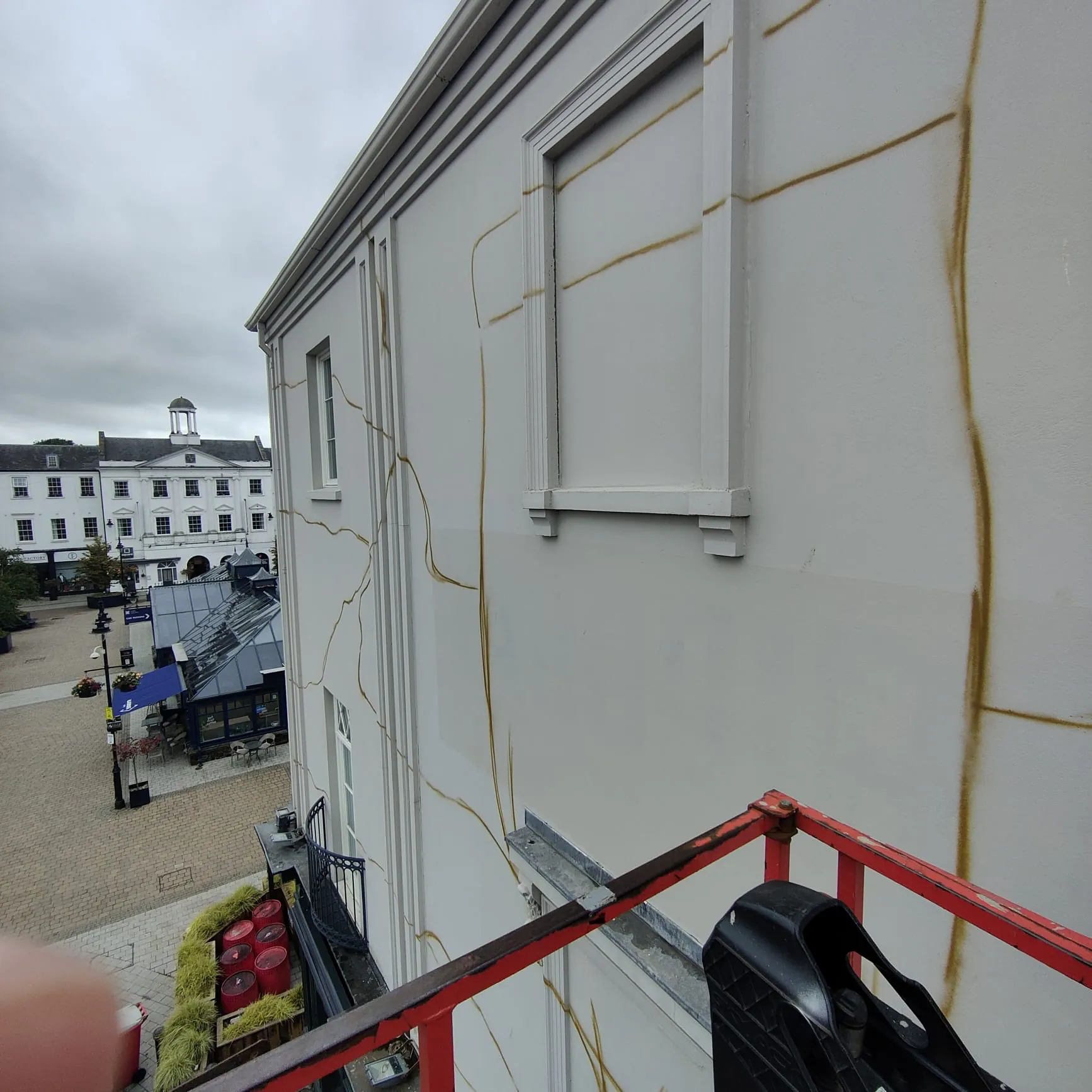 Gold guide lines sketched across The Lark’s white wall, seen from the cherry picker above the square.