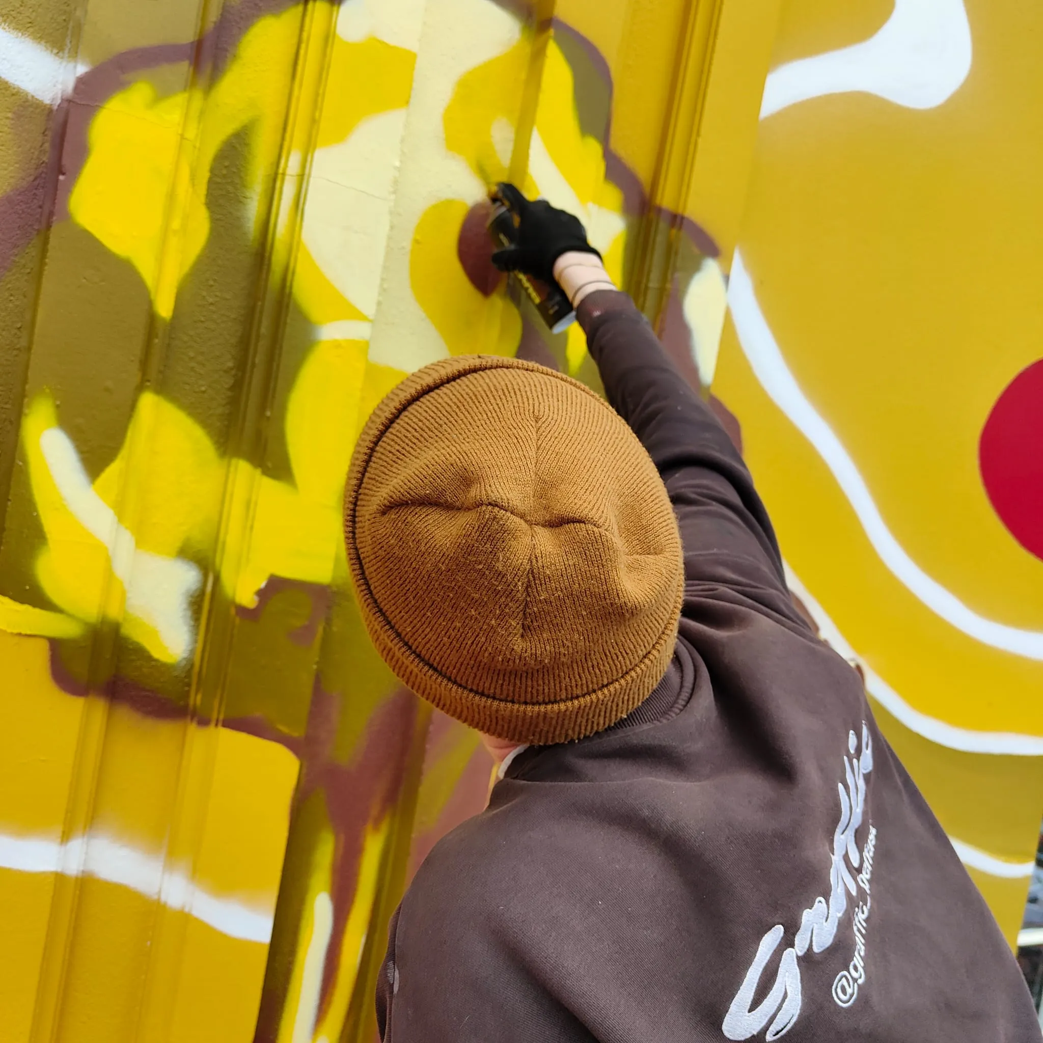 A painter spraying white highlights over the yellow shapes of the Madrí mural.