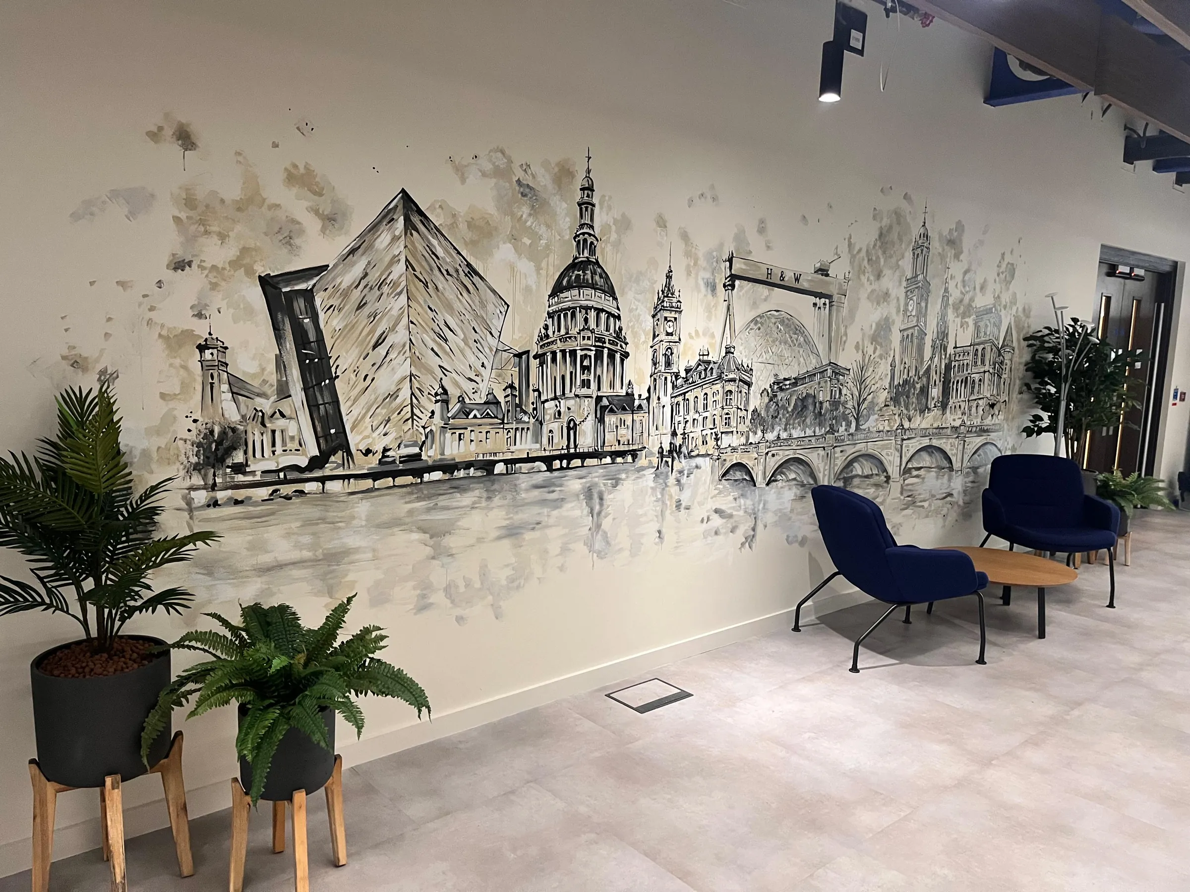 A hand-painted Belfast skyline in black and sepia washes along an office wall at TP ICAP, with Titanic Belfast and City Hall above the river’s bridges.