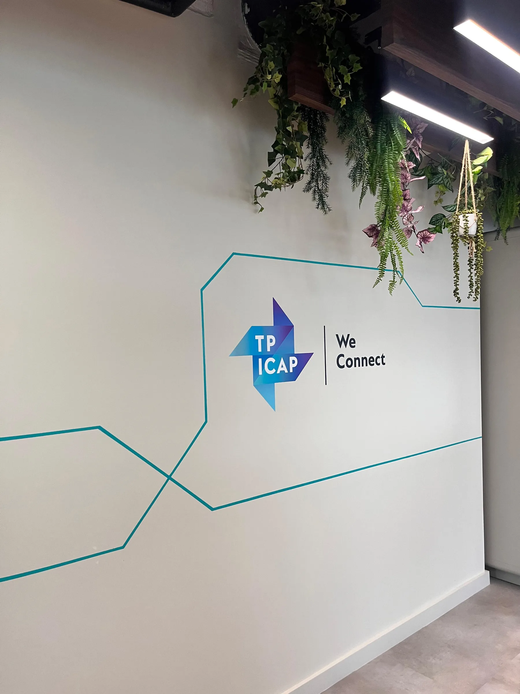 The TP ICAP logo and “We connect” painted on a white wall, with teal lines running across it.