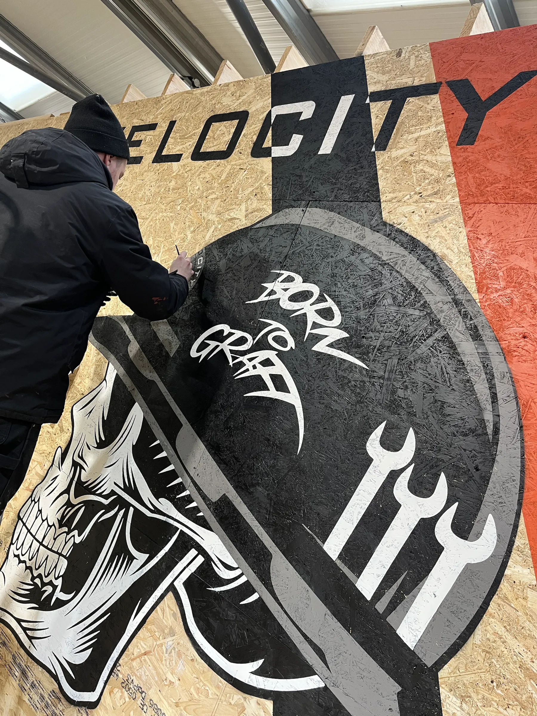 A close-up of a painter detailing the skull’s “Born to Graft” hard hat.