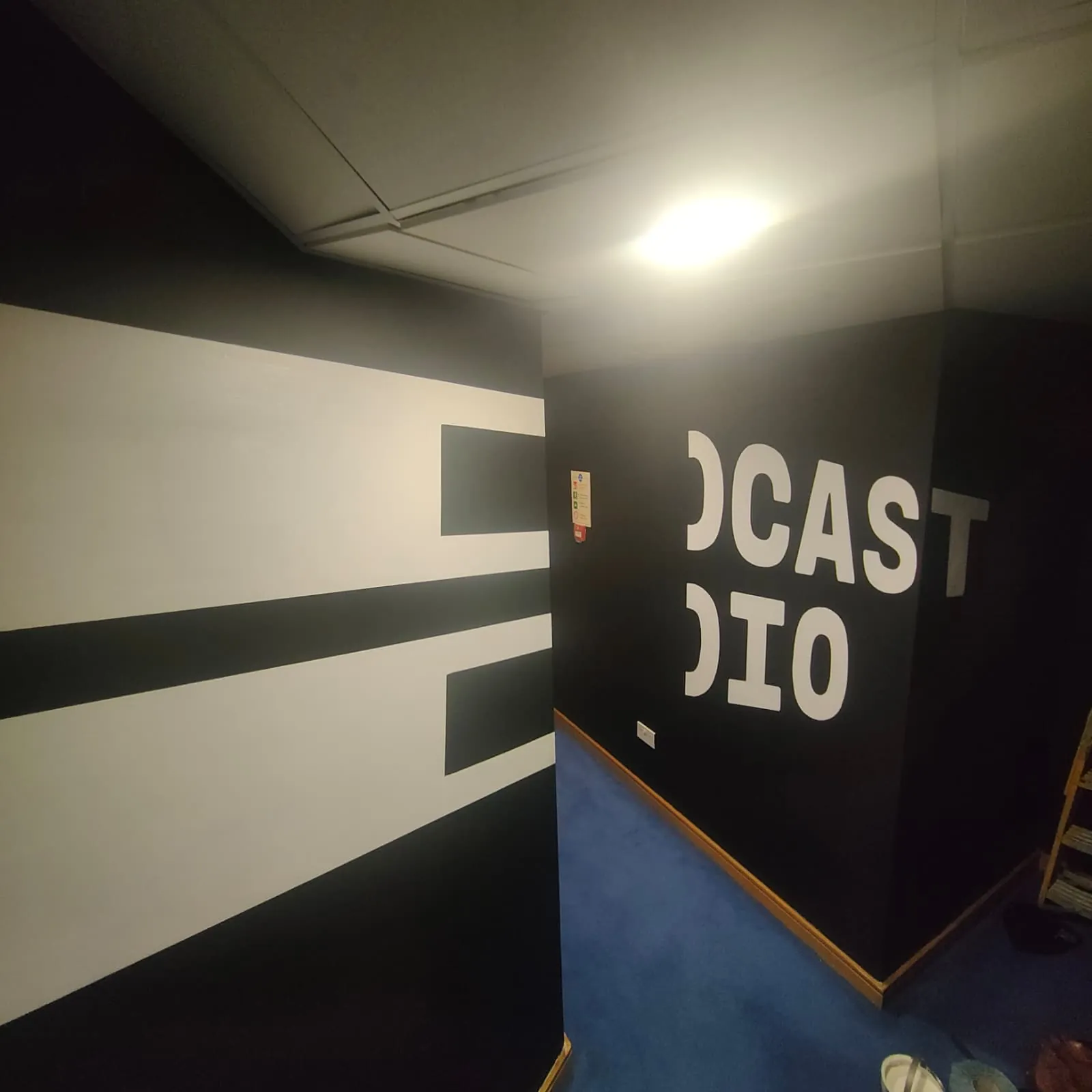 A white stripe and the end of “Podcast Studio” painted round a corner of the black corridor.