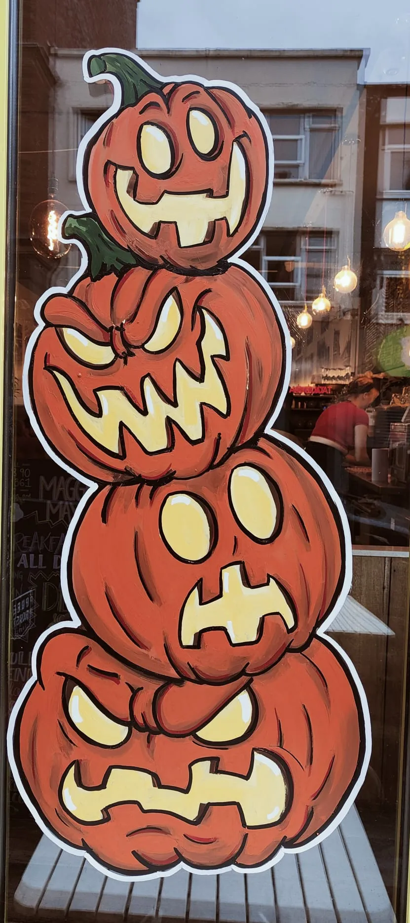 Four stacked jack-o’-lanterns painted on a glass door.