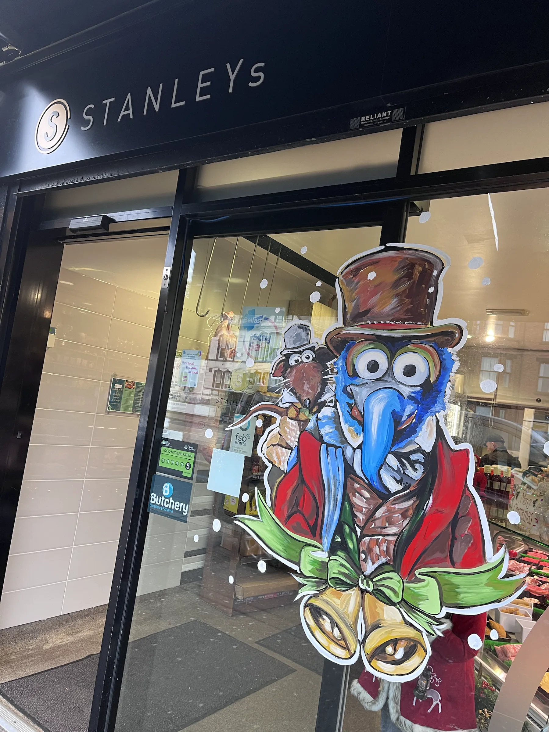 Gonzo and Rizzo from The Muppet Christmas Carol painted on the glass door of Stanley’s butchers, with brass bells and a holly bow.