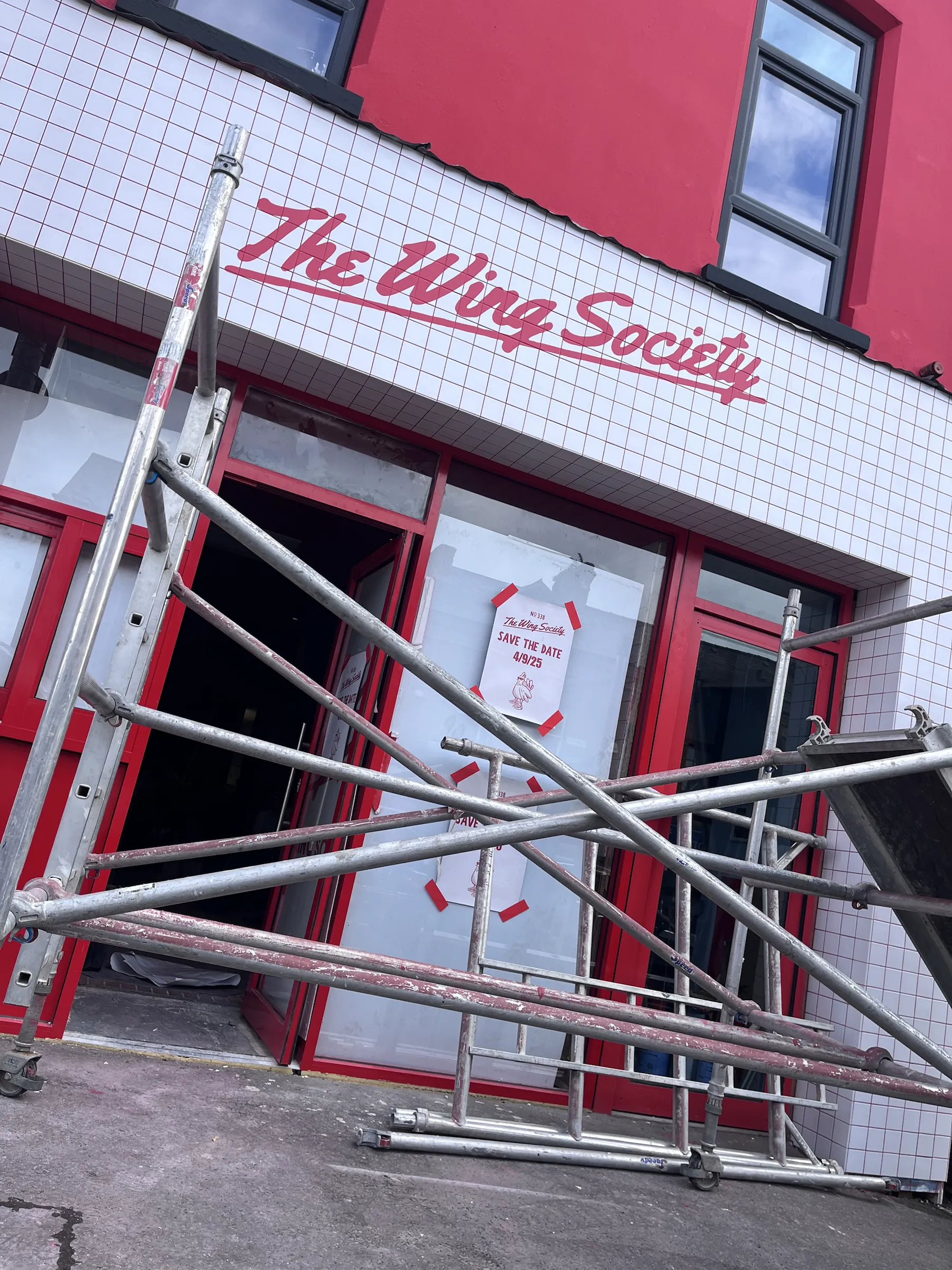 Scaffolding in front of the new red and white shopfront, The Wing Society’s name already painted on the fascia.