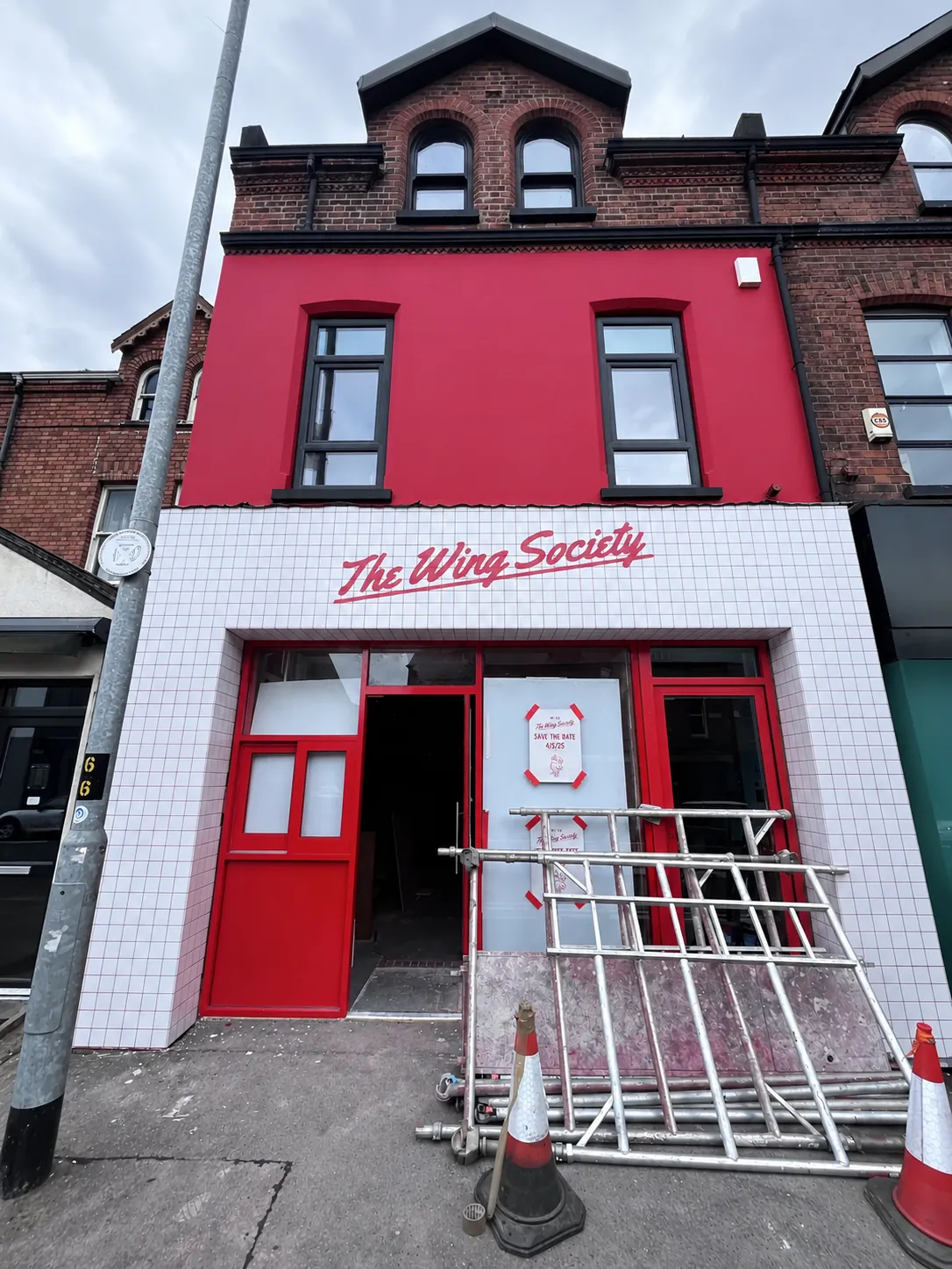 The Wing Society’s new frontage with its name painted in red script on the white-tiled fascia below a red upper floor, scaffolding and traffic cones still outside the door.